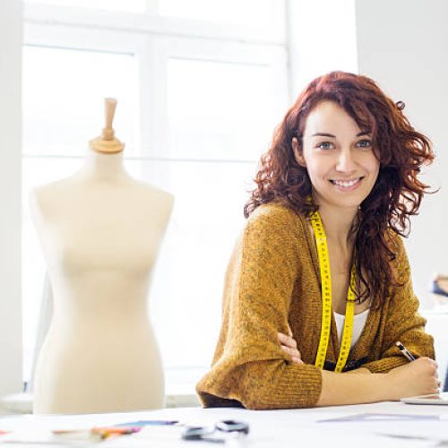 Beautiful young female designer sitting at a table in clothing design studio
